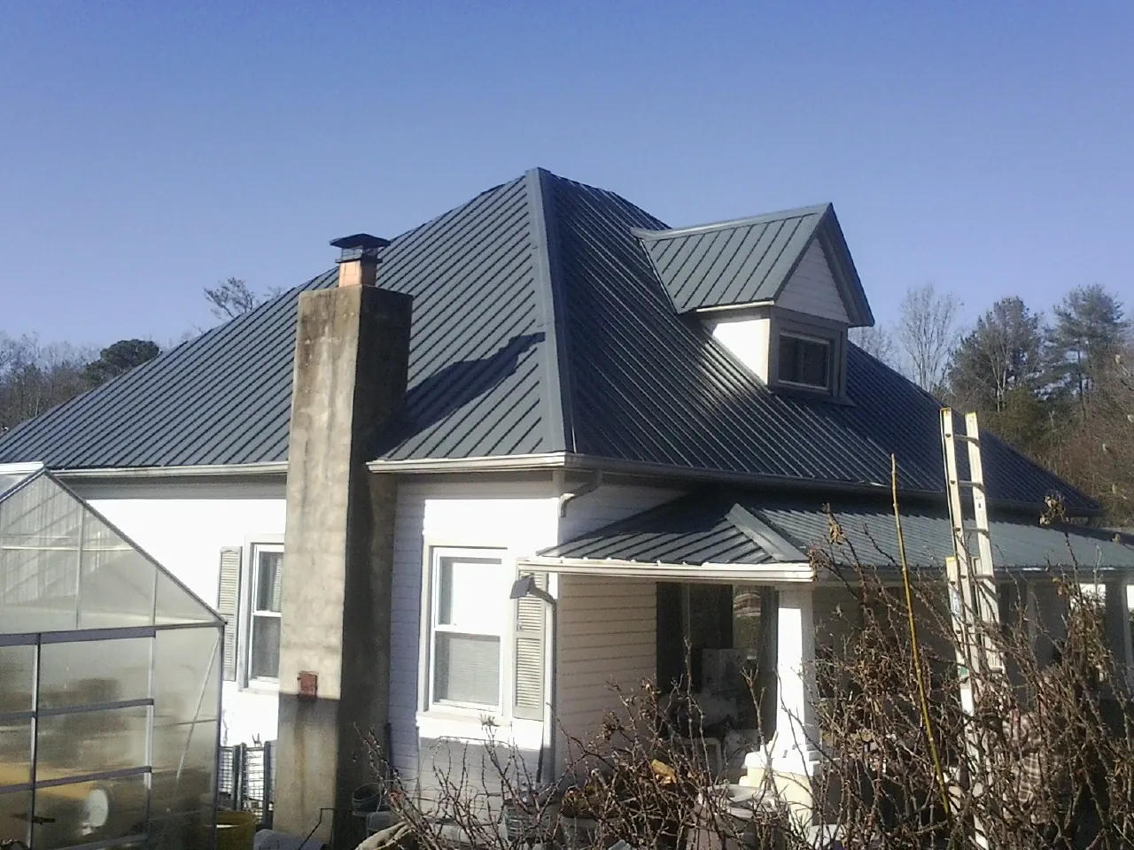 Dark blue standing seam metal roof on a white farmhouse with dormer — Slate & Tile Roof Repair by Roofing Brothers in Chadbourn