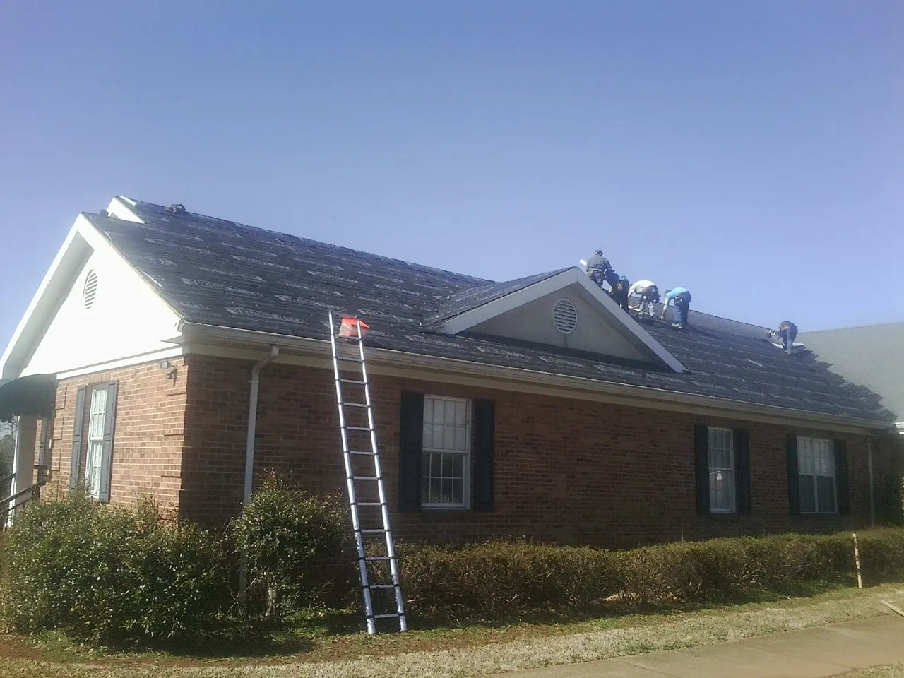 Crew tearing shingles off a brick ranch roof with a ladder set — Metal Roof Repair work by our crew in Chadbourn