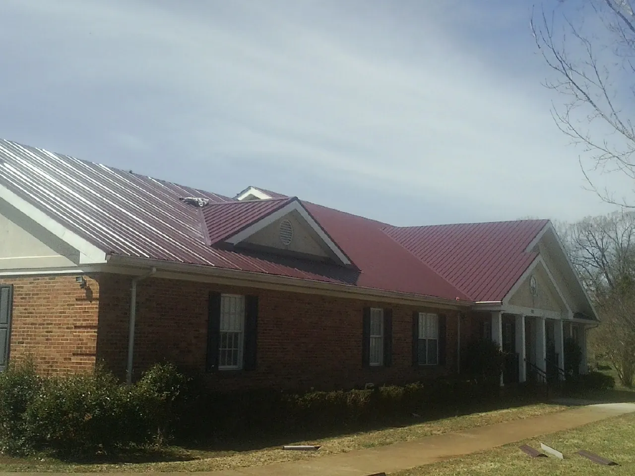 Red metal roof with gabled entries on a long brick building, from a Hail Damage Roof Repair job in Chadbourn