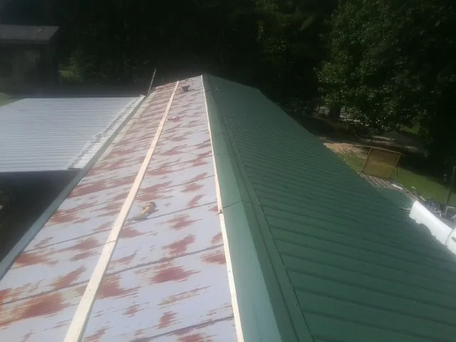Old rusted panels beside newly installed green metal roofing — Wind Damage Roof Repair by Roofing Brothers in Chadbourn