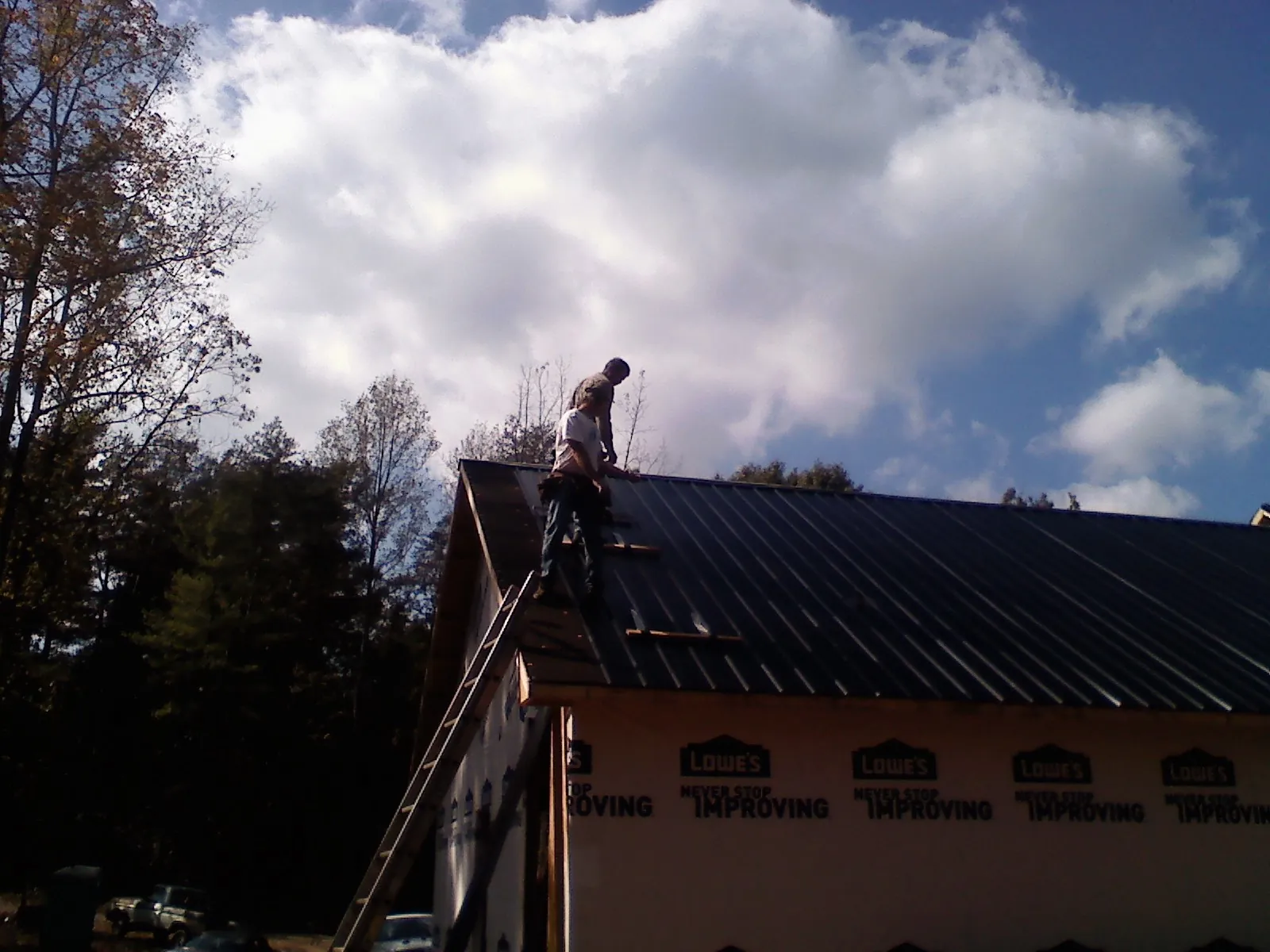Roofer fastening dark metal panels high against a cloudy sky, from a Roof Inspection job in Chadbourn
