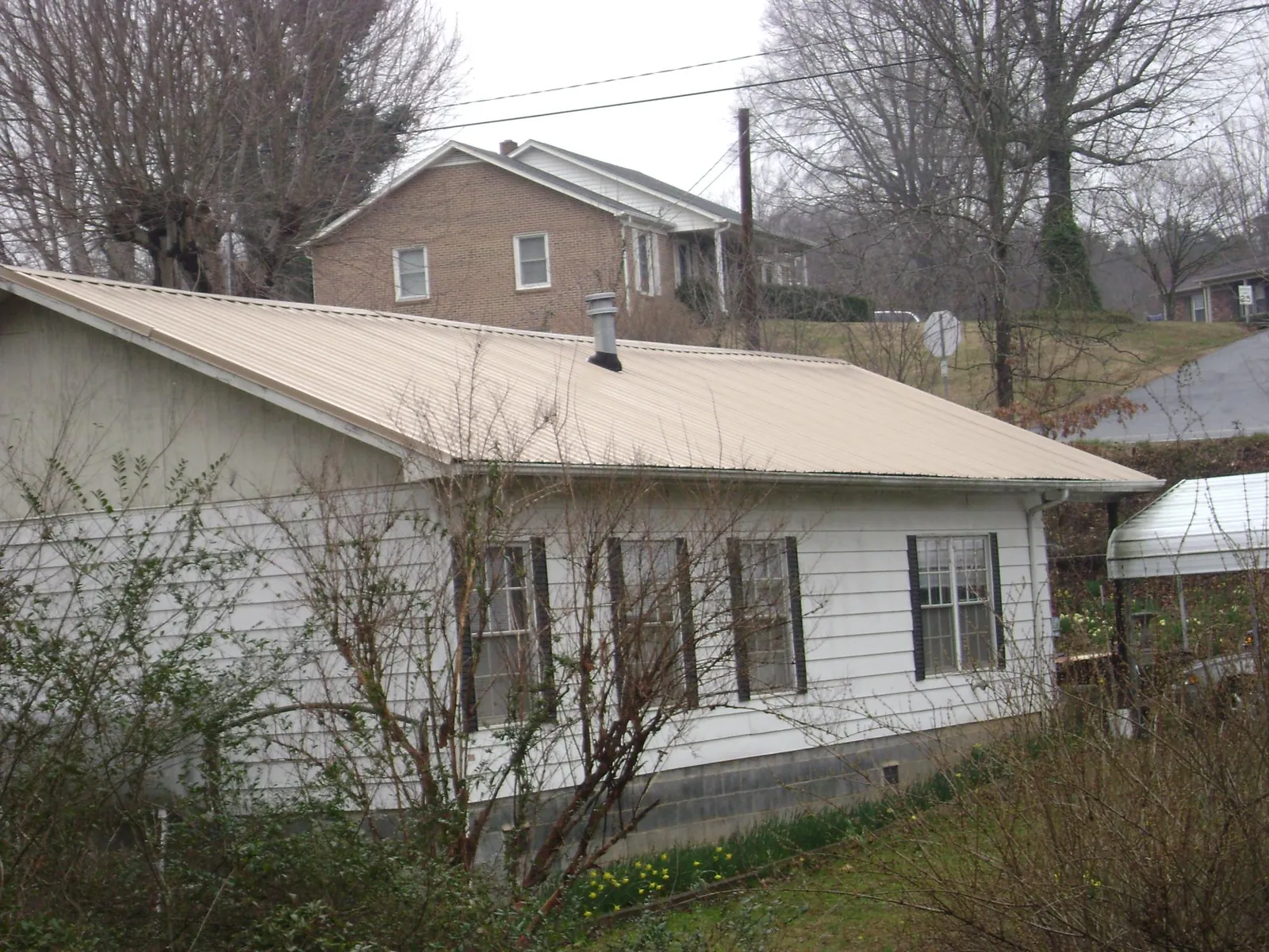 Tan metal roof on a white sided house set into a hillside — Commercial Roofing by Roofing Brothers in Chadbourn