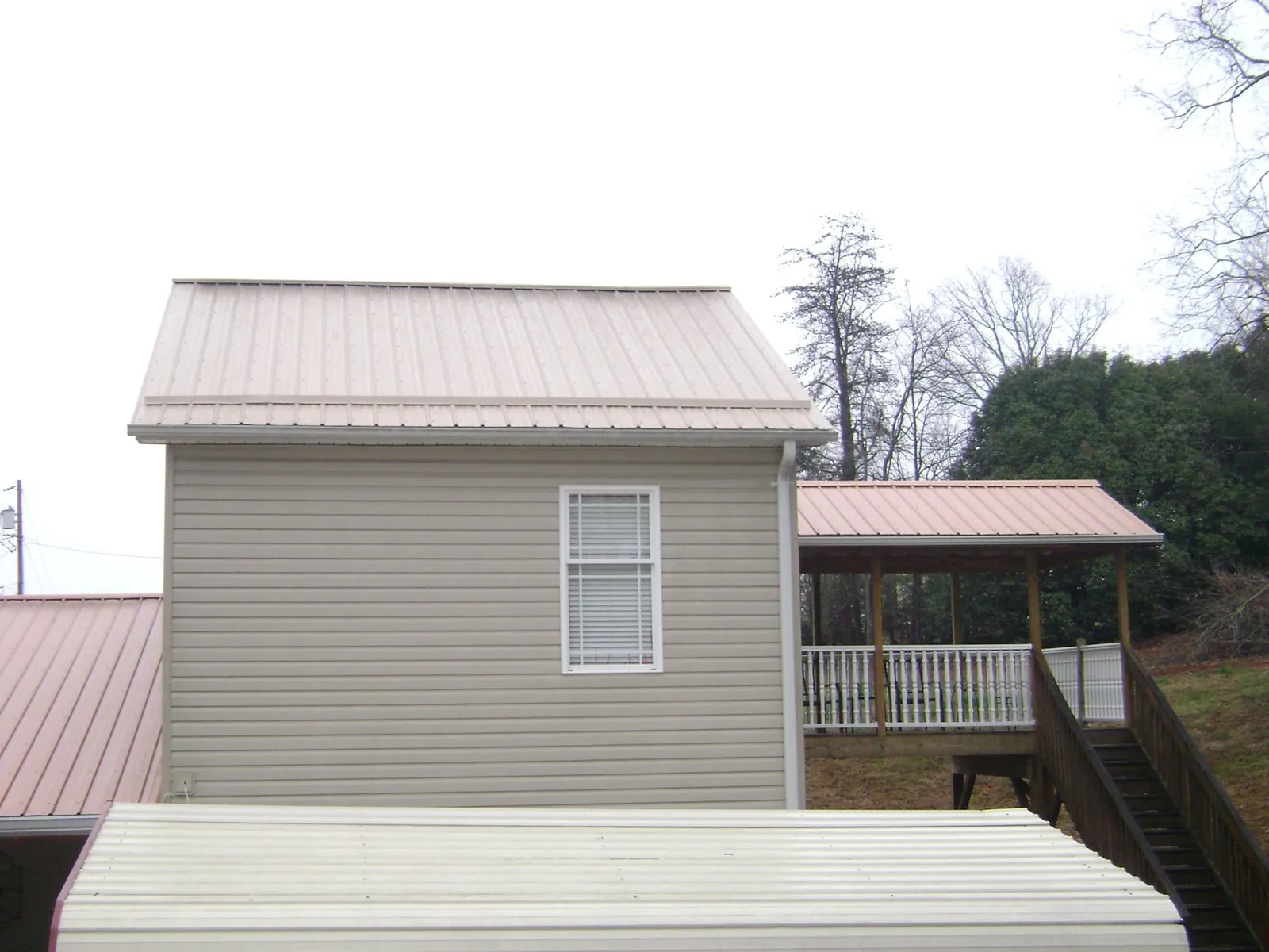 Tan metal roofs on a two story addition and attached porch, from a Roof Replacement job in Chadbourn